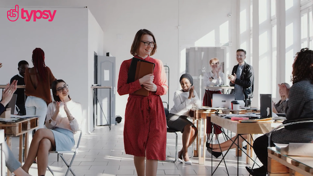 Confident woman in red dress smiling in office surrounded by team