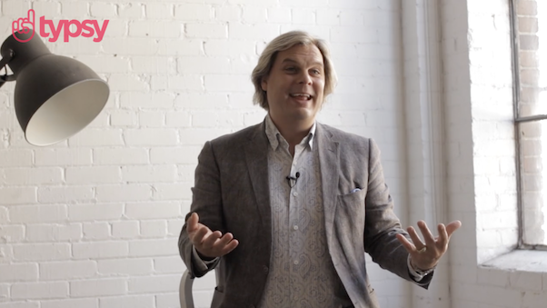 Man standing against a white brick wall presenting a seminar.