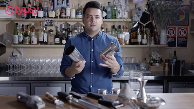 A young man stands at a bar with a shaker in preparation for making a drink.