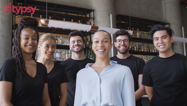 A group of people stands in front of the bar where they work.