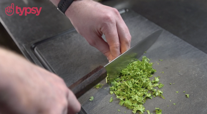 A man's hands holding a knife chops parsley.